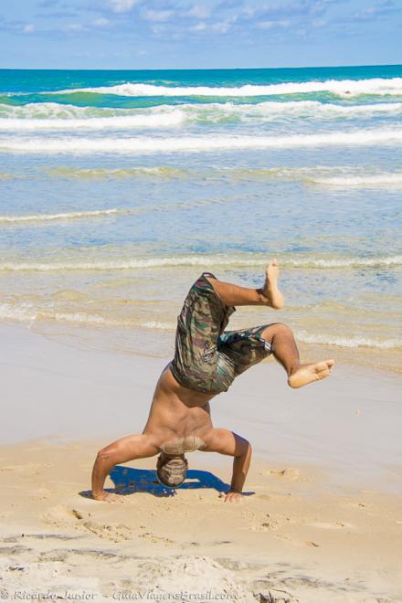Imagem de um rapaz de cabeça pra baixo nas areias da Praia de Jeribucaçu.